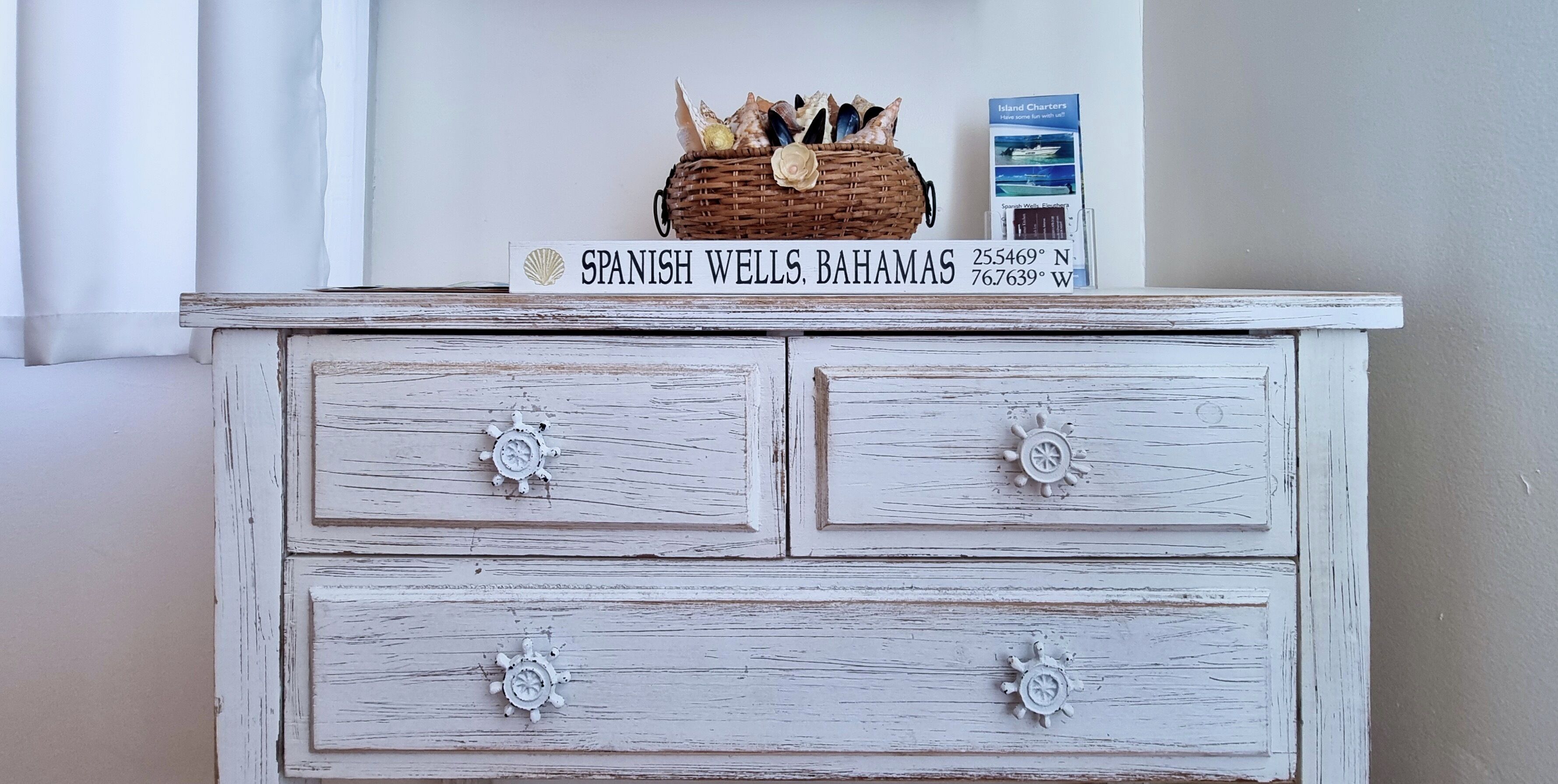A white dresser with nautical-themed knobs and a sign reading "SPANISH WELLS, BAHAMAS" above it.