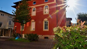 A red building with arched windows and a stone base, surrounded by greenery. - Nine Rooms Suites (Trento)