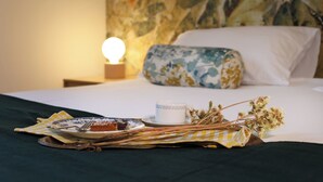 A neatly made bed with a floral pillow, a bedside table with a lamp, and a breakfast setup including a plate, a cup, and some flowers. - Nine Rooms Suites (Trento)