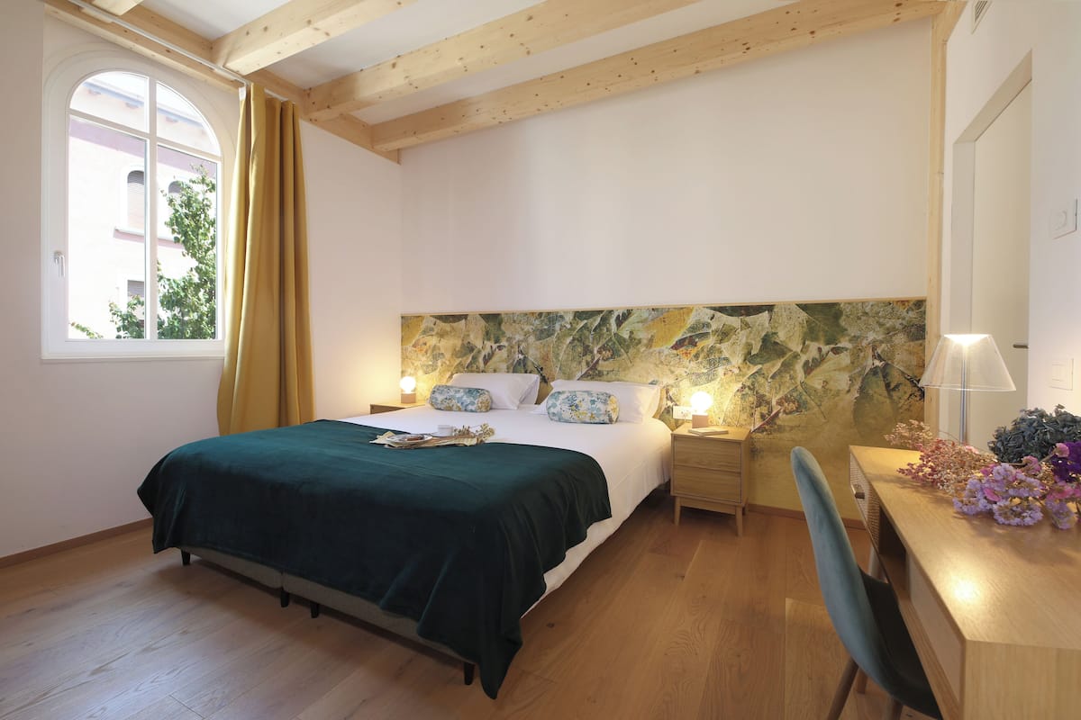 A bedroom with a bed, wooden headboard, bedside tables, a desk, and a chair.