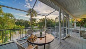 A covered outdoor area with a glass balustrade, a round table, and chairs, overlooking a river and lush greenery. - Siesta Key Complete House - Pool - Jacuzzi - 3 Bedroom - 2 Bath - Screened Patio (Sarasota)