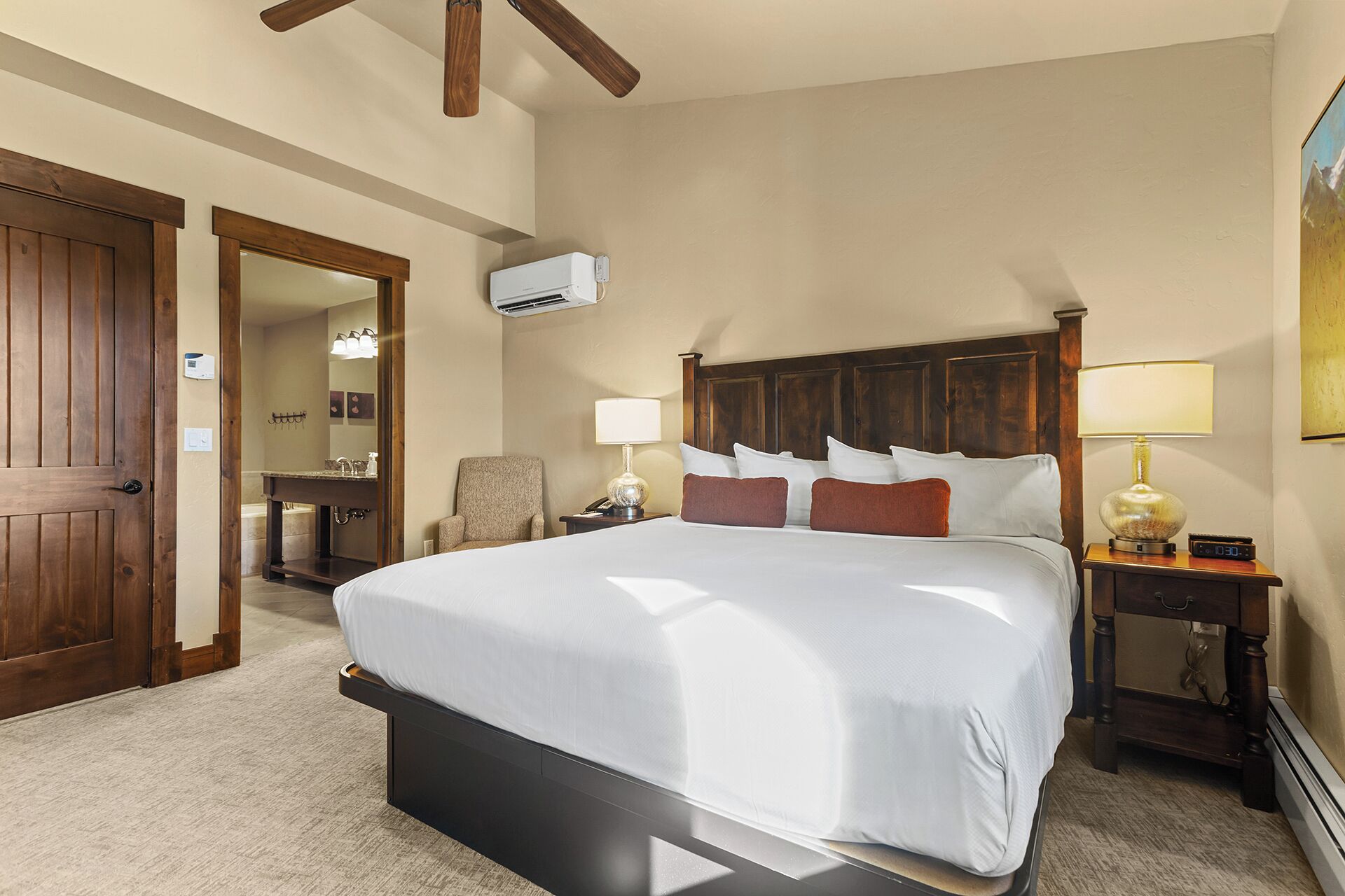 Una camera d'albergo con un letto grande, testiera in legno, lampade sui comodini, una sedia, una scrivania e un condizionatore d'aria.