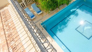 A swimming pool with a clear blue waterline, surrounded by a tiled deck and a metal railing.