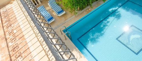 A swimming pool with a clear blue waterline, surrounded by a tiled deck and a metal railing.