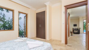 A bedroom with a bed, two windows, a wardrobe, and a view of a living area.