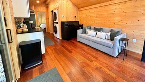 L’intérieur d’un chalet accueillant, avec un revêtement mural en bois, un canapé, une petite table et un lave-linge.