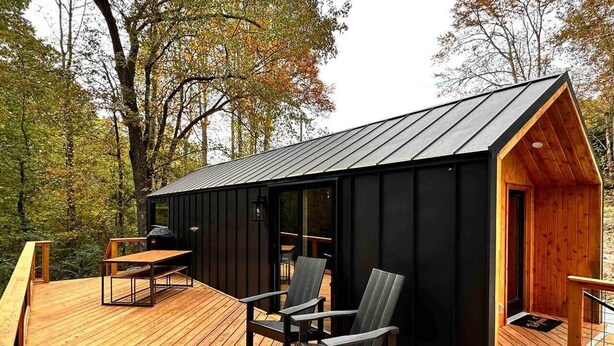 Une cabane dotée d’une terrasse en bois, d’un coin repas avec des chaises et d’un petit porche.