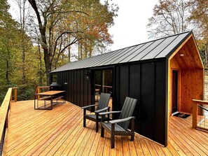 Een chalet met een houten terras, een eethoek met stoelen en een klein voortuintje.