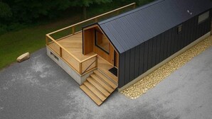 Une cabane moderne dotée d’une terrasse en bois, d’un porche couvert et d’une façade noire.