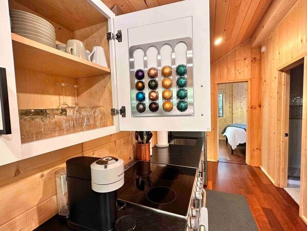 Een keuken met een ingebouwde koffieapparaat, een fornuis en een plank met glazen.