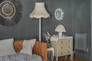 Une pièce avec un mur sombre, un miroir rond, une lampe, une commode et un radiateur.