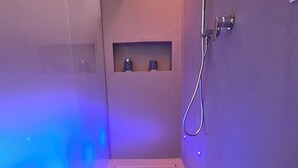 A small, dimly lit room with a shower, a sink, and a shelf with bottles. - La Piazzetta, Luxury Charming Balcony Room, a few steps from the beach  (Polignano a Mare)