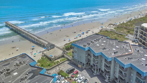 A coastal hotel with a beach view, a pier, and a parking area.