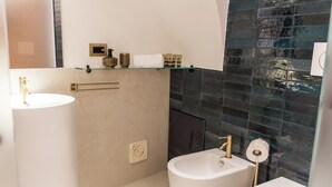 A bathroom with a white sink, a bidet, and a toilet. There is a shelf with toiletries and a towel.