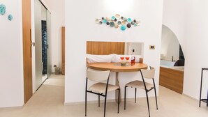 A modern dining area with a round table, two chairs, a decorative wall piece, and a view into the kitchen.