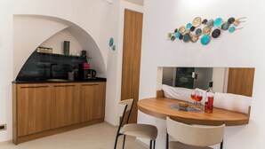 A compact kitchen with a wooden countertop, a sink, and a coffee machine. There is a round wooden table with two chairs and a decorative wall piece above it.