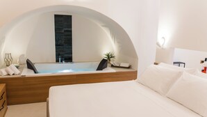 A modern hotel room with a large arched window, a bathtub, a bed, and a bedside table with a bottle.
