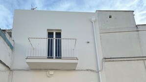 A two-story building with a balcony, a door with shutters, and a small window.