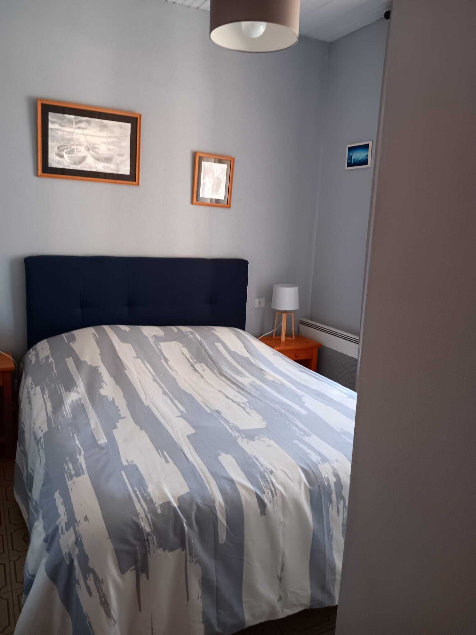 Un dormitorio con una cama grande, una mesita de noche, una lámpara y dos cuadros en la pared.
