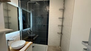 Un baño moderno con ducha envuelta en vidrio, un lavabo blanco con encimera de madera y un perchero para toallas.