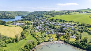 An aerial view of a coastal village with houses, a small harbor, and surrounding green fields. - Water Edge House Boathouse (Dartmouth)