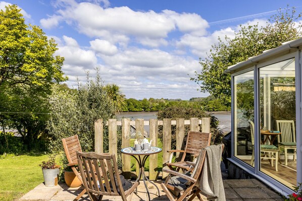 An outdoor patio with a wooden table and chairs, a potted plant, and a view of the countryside. - Water Edge House Boathouse (Dartmouth)