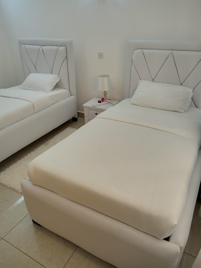 A hotel room with two beds, a nightstand, and a lamp.