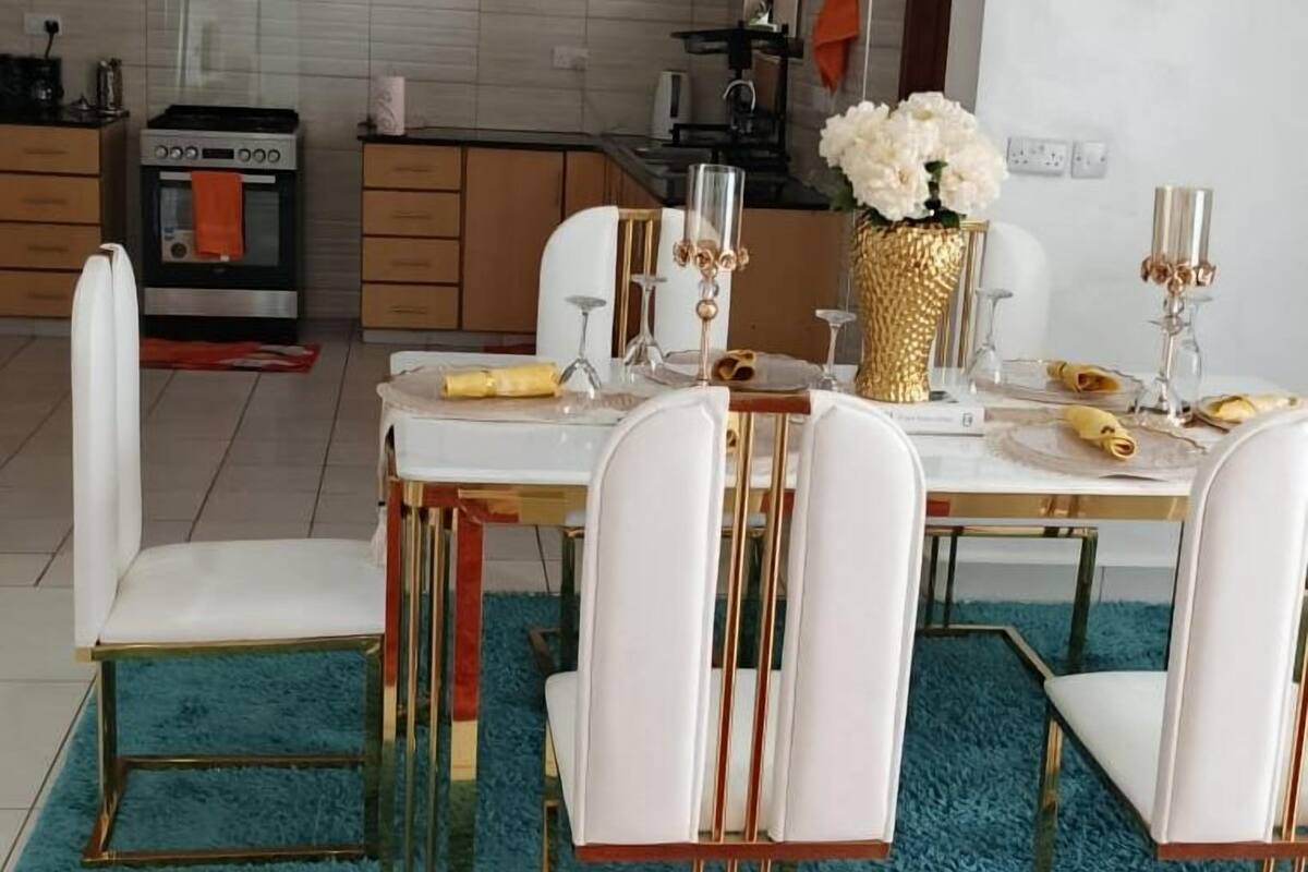 A modern kitchen with wooden cabinets, a built-in oven, and a dining area with a white table set for six.