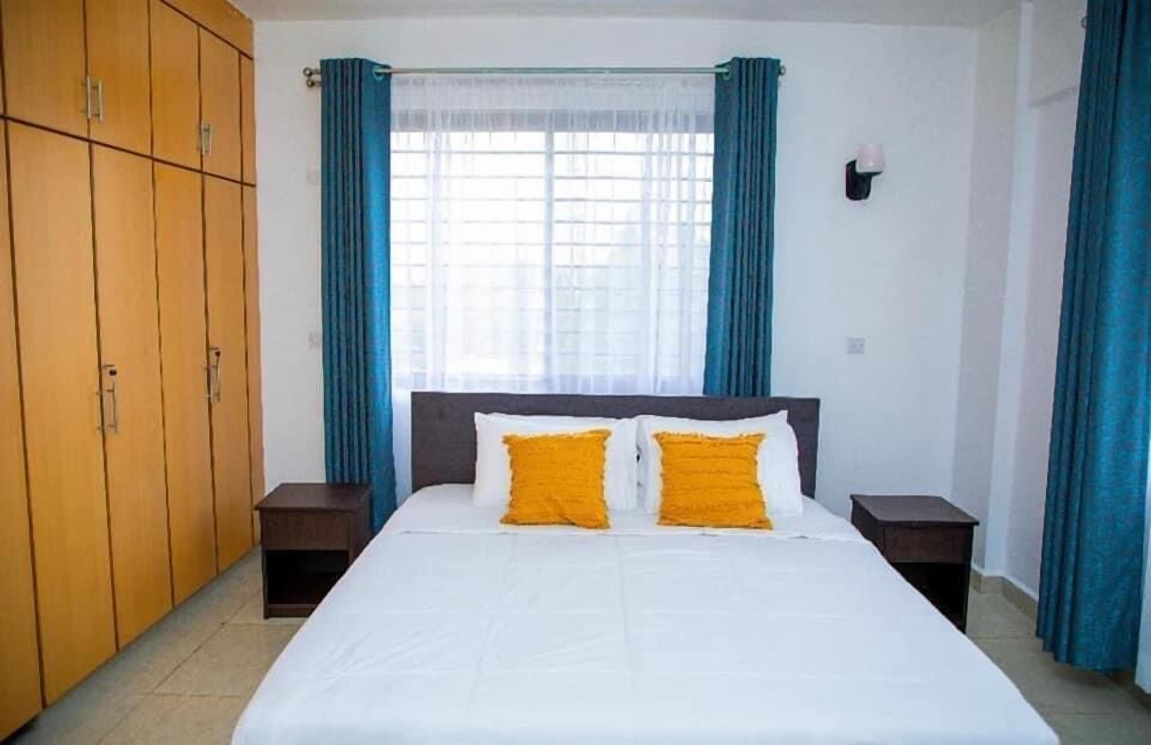 A bedroom with a large bed, wooden wardrobe, and a window with curtains.