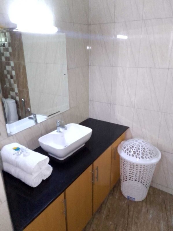 Un baño con un lavamanos blanco, un espejo y una cesta de ropa blanca.