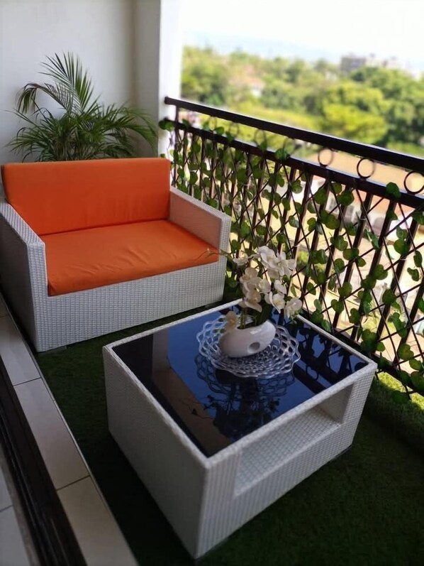 Un balcon avec un canapé en osier, une petite table ornée d’un vase de fleurs et une vue sur la verdure.