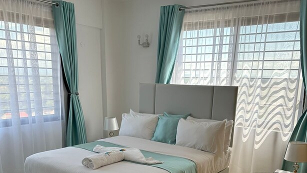 Ein modernes Schlafzimmer mit einem großen Bett, weißer Bettwäsche, lindgrünen Vorhängen und einem flauschigen Teppich.
