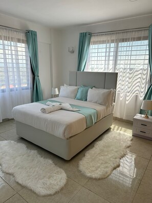 Une chambre moderne avec un grand lit, une literie blanche, des rideaux turquoise et un tapis moelleux.