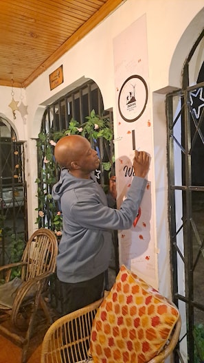 A person writing on a wall with a logo and text, a star decoration, a chair, and a window with bars. -  Indovu Wellness Retreat (Nairobi)