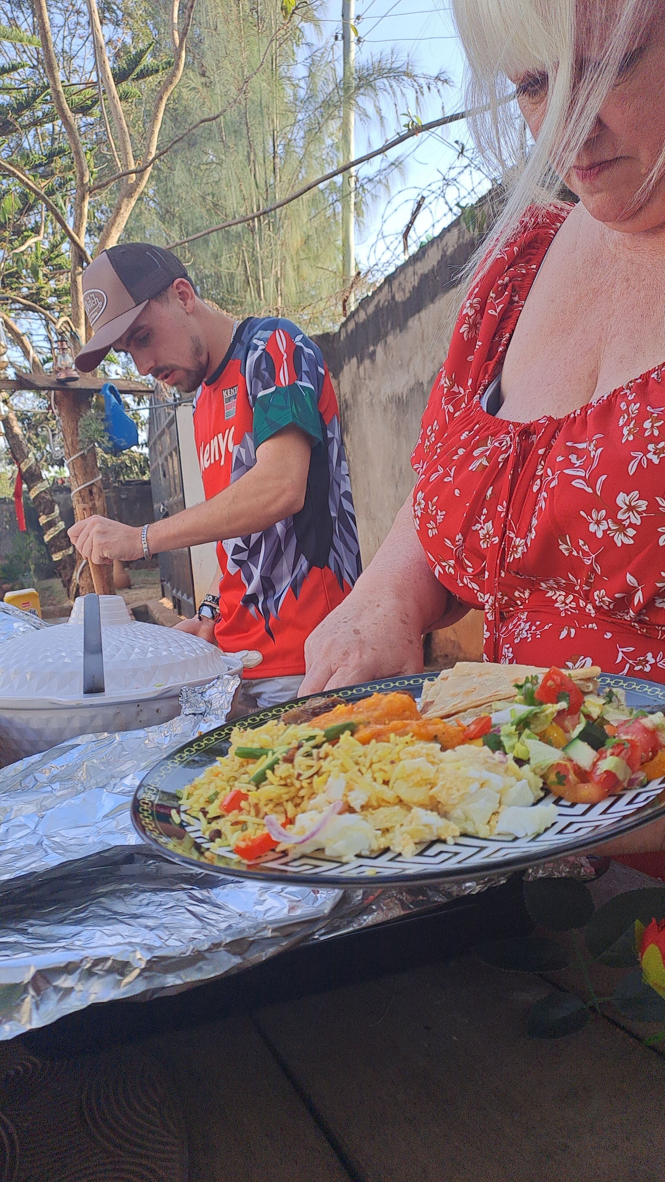 A person cooking outdoors with a grill and foil-covered food on a table.