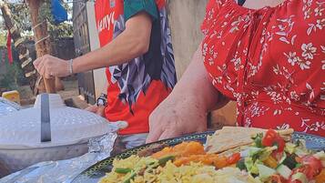 A person cooking outdoors with a grill and foil-covered food on a table.