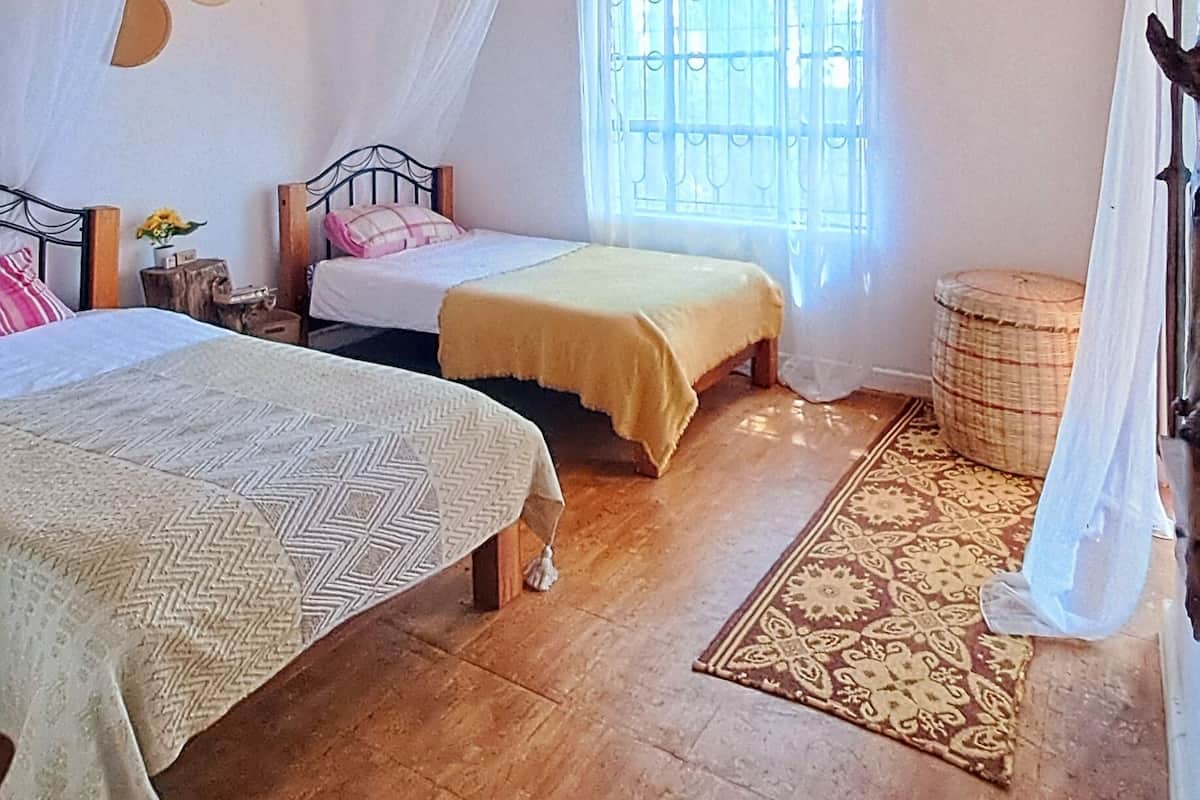 A cozy room with a wooden ceiling, two beds, a window with bars, and a small round table.