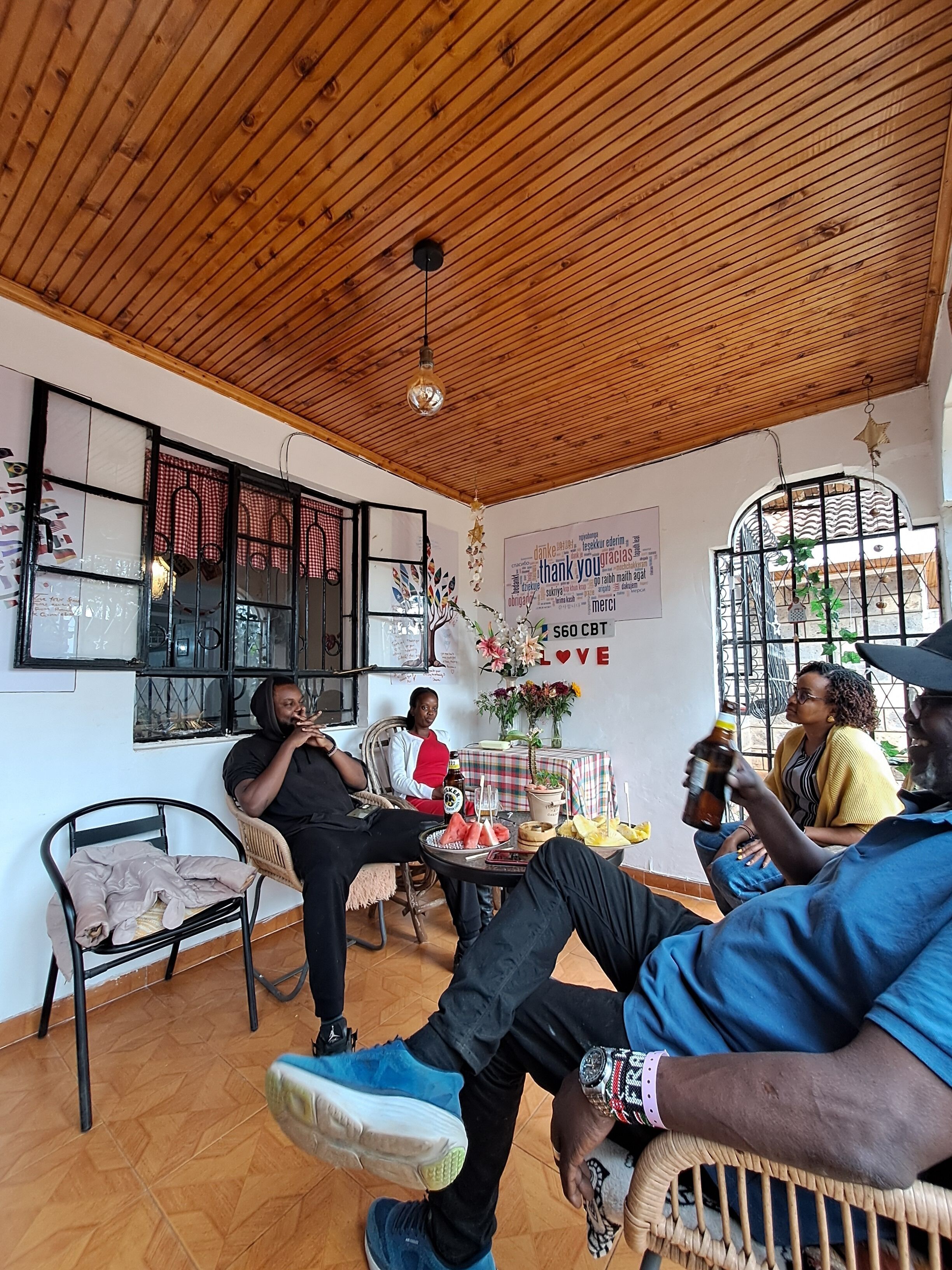 A room with wooden ceiling, a table with drinks, chairs, and a window with decorative elements.