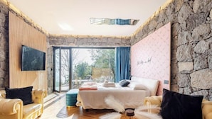 A bedroom with a stone wall, a bed with white bedding, a large window, and a view of the outdoors.