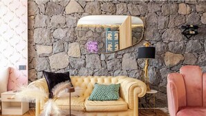 A living room with a stone wall, a tufted sofa, a round wooden coffee table, a pink armchair, and a floor lamp.