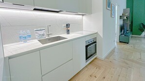 A modern kitchen with a built-in oven, a stainless steel sink, and a marble countertop.