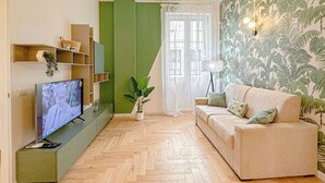 A living room with a television, a sofa, a plant, and a wall with a leaf pattern.