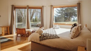 Un dormitorio con una cama grande, una silla, una mesita y dos ventanas con cortinas.