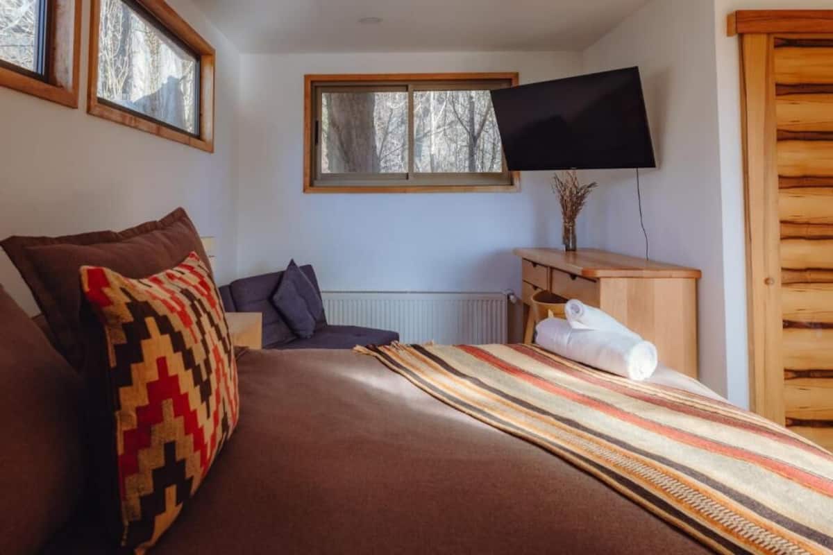 A bedroom with a bed, a television mounted on the wall, and a window with a view of trees.