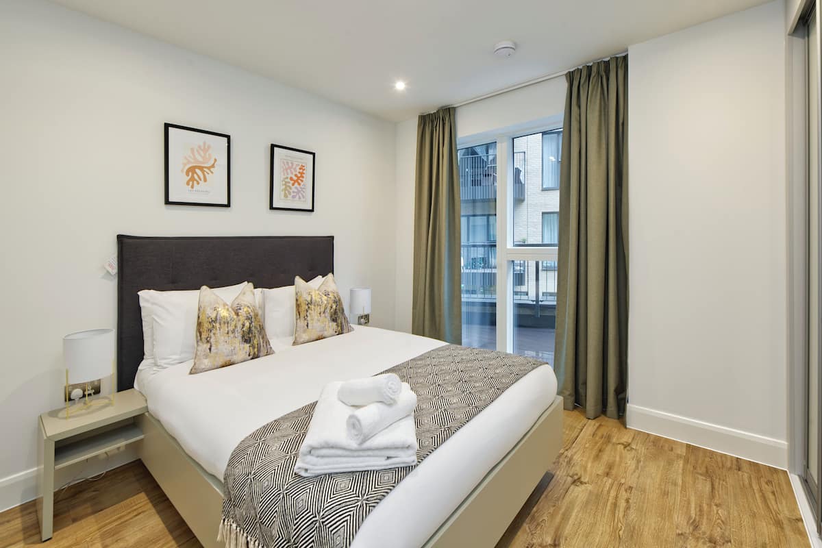 Une chambre d’hôtel moderne avec un grand lit, une table de chevet, une fenêtre avec des rideaux et deux œuvres d’art encadrées accrochées au mur.