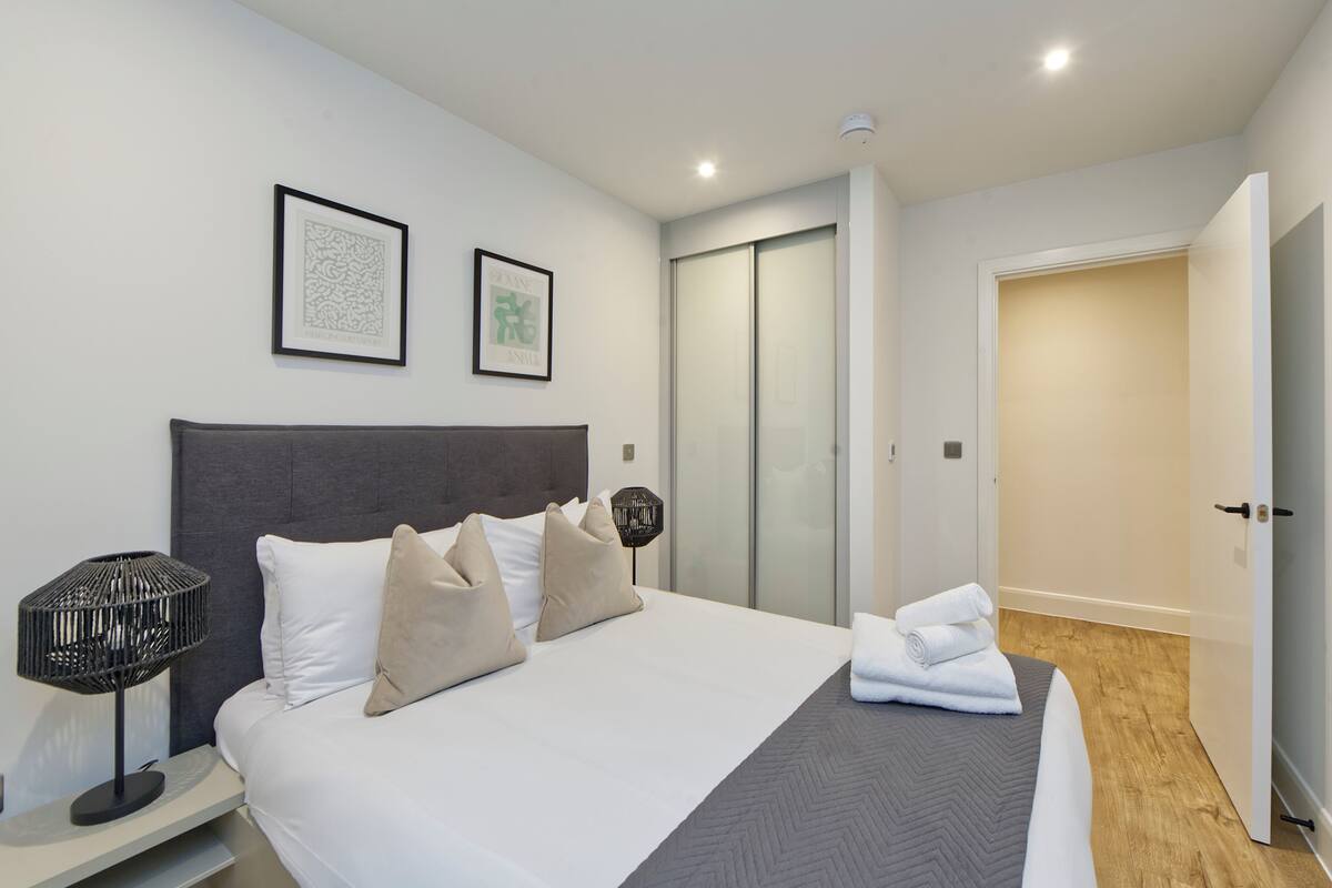 Une chambre d’hôtel moderne dotée d’un grand lit, d’une table de chevet avec une lampe, d’une armoire et d’une porte donnant sur une autre pièce.