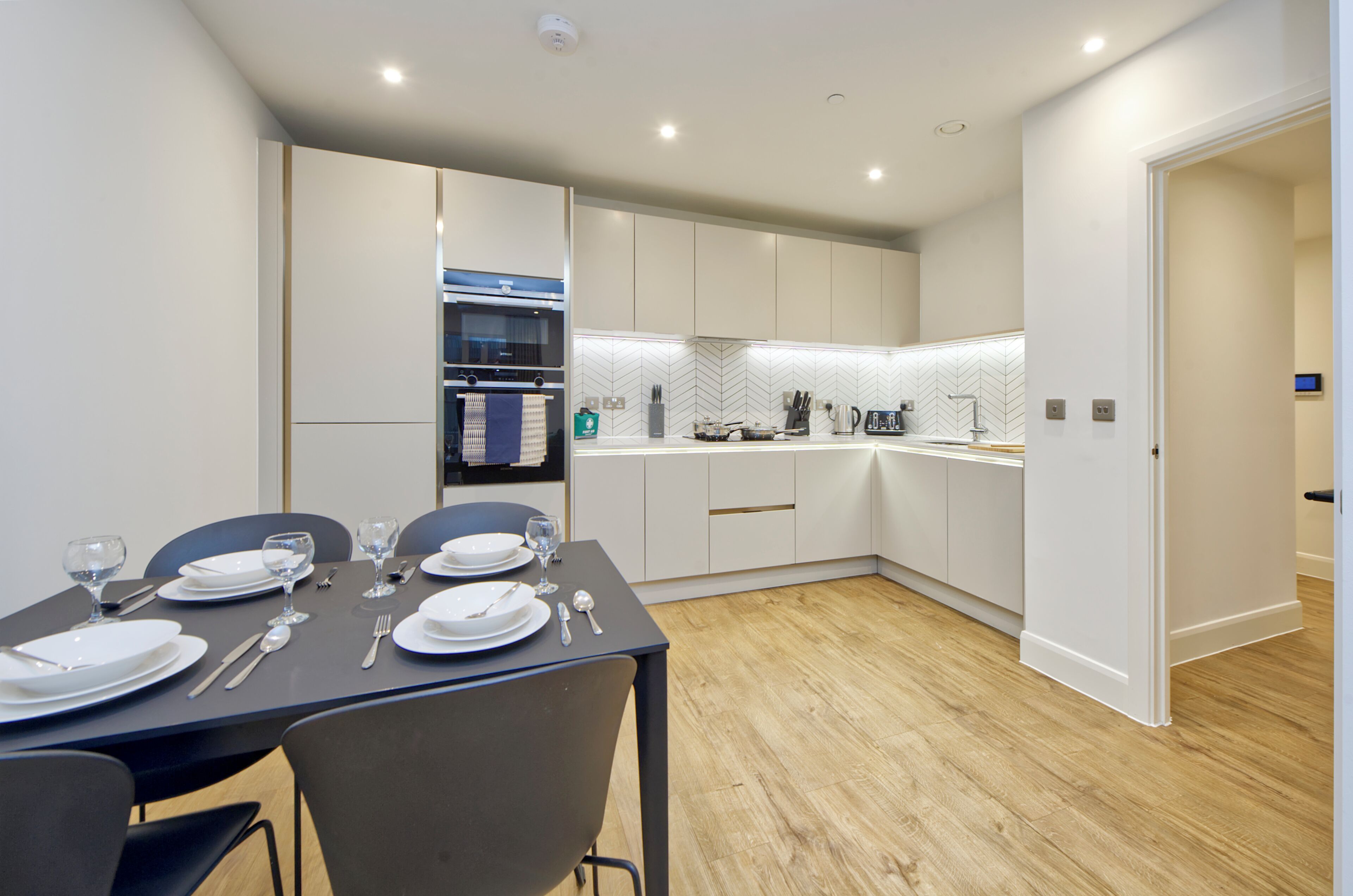 A modern kitchen with white cabinets, a built-in oven, and a herringbone backsplash.