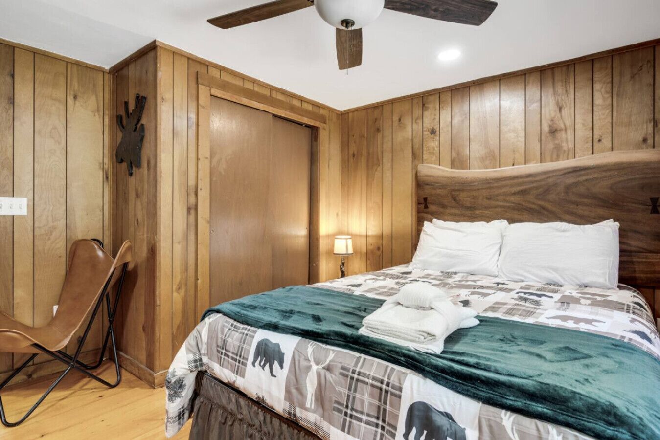 Ein Zimmer mit Holzwänden, einem Bett, einem Sessel und einem Deckenventilator.