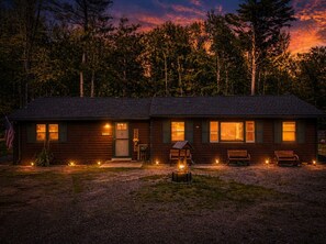 A wooden cabin with a porch, a flag, and a fire pit.