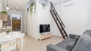 A modern living room with a grey sofa, a TV on a white stand, a dining area with a table and chairs, and a wooden staircase. - GuestReady - Cozy stay near Malvarrosa Beach (Valencia)